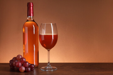 Rose wine in glass, bottle and grapes on wooden table against brown background, space for text