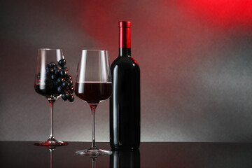 Red wine in glass, bottle and grapes on black table against color background. Space for text