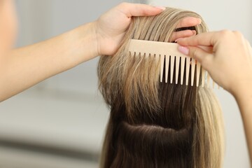Fototapeta premium Hairdresser combing woman's hair in salon, closeup