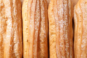 Tasty eclairs with powdered sugar as background, top view