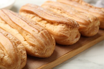 Fototapeta premium Tasty eclairs with powdered sugar on white marble table, closeup