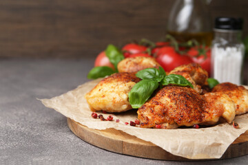 Tasty roasted chicken thighs with basil, spices and tomatoes on grey table, closeup. Space for text