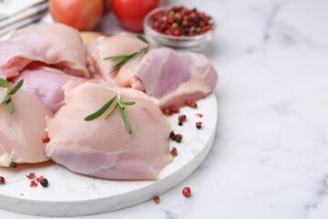 Raw chicken thighs with rosemary, peppercorns and tomatoes on white marble table, closeup. Space for text