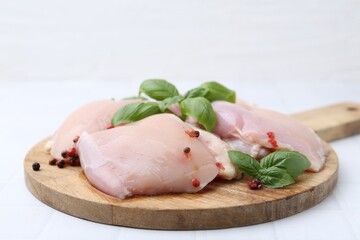 Raw chicken thighs with basil and peppercorns on white tiled table, closeup