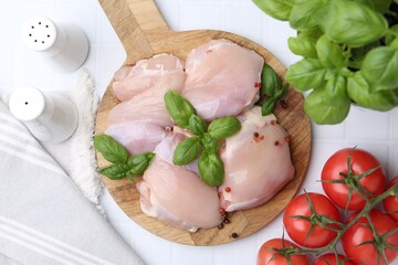 Raw chicken thighs with basil, peppercorns and tomatoes on white tiled table, flat lay