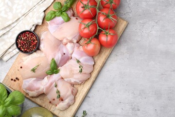 Raw chicken thighs with herbs, peppercorns and tomatoes on light table, flat lay. Space for text