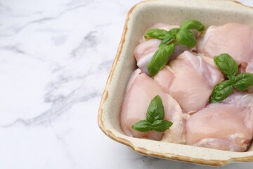 Raw chicken thighs with basil in baking dish on white marble table, closeup. Space for text