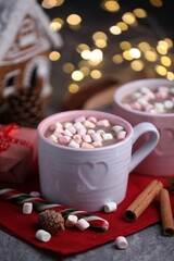 Tasty cocoa with marshmallows, cinnamon and Christmas decor on grey table against blurred lights, closeup