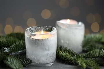 DIY Christmas lantern. Burning ice candles and fir branches on grey table against blurred lights, closeup. Bokeh effect © New Africa