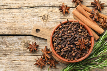Mulled wine spices. Cloves in bowl, anise stars and fresh rosemary on wooden table, flat lay. Space for text