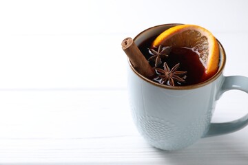 Tasty mulled wine with spices in mug on white wooden table, closeup. Space for text