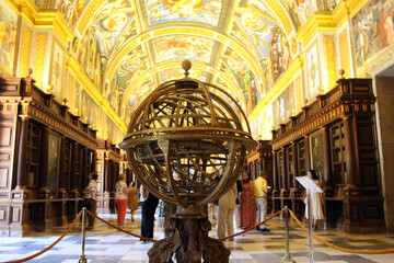 Globe in library of El Escorial with big hall, vaulted ceilings, wall paintings, and shelves of ancient manuscripts. Photographed in July 2024.