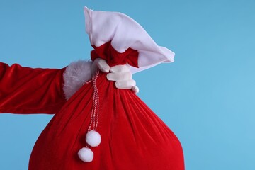 Santa Claus holding sack on light blue background, closeup with space for text. Merry Christmas and...