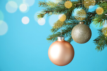 Christmas balls hanging on fir tree branches against light blue background with blurred lights,...