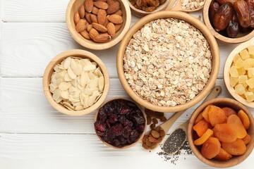 Making granola. Oat flakes, dried fruits and other ingredients on white wooden table, flat lay