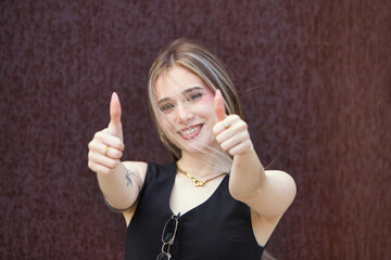 blonde woman with light eyes, young and beautiful, holds up the thumb of her two hands and makes a...