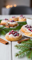 Close-up of pastry with red berries and sugar powder, placed on white wooden table with cinnamon and fir branch, representing festive, holiday treat