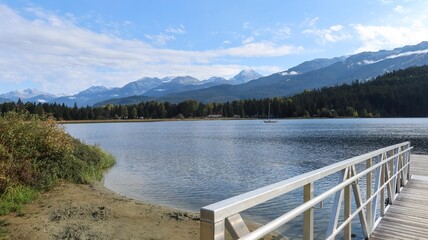 wooden deck dock by the waterside of Rainbow Park, Whistler, British Columbia, Canada: the trail and park along Rainbow Lake on a good weather day with blue sky and reflection of trees