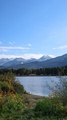 pine trees lined up on the opposite side of the lake in Rainbow Park, Whistler, British Columbia, Canada on a good weather blue sky day and snow on mountain