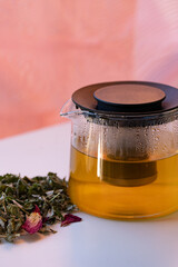 Herbal mix on a plate sits beside a glass teapot; soft focus, clean composition and warm tones suggest natural tea wellness ritual and balanced, approachable lifestyle at home.