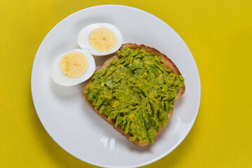 Avocado toast with boiled eggs on white plate on yellow background