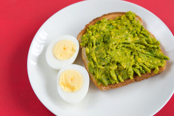 Avocado toast with boiled eggs on white plate over red background