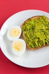Avocado toast with boiled eggs on white plate over red background