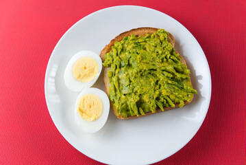 Avocado toast with boiled eggs on white plate over red background