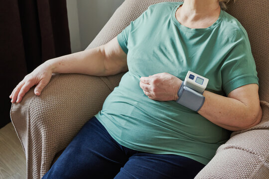 An elderly, overweight woman using digital wrist monitor to measure blood pressure, focusing on health and self-care