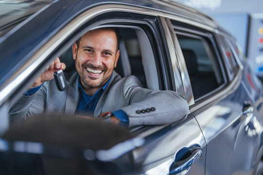 Smiling Businessman in Suit Holding Car Key Inside Vehicle at Dealership Showing Customer Service Interaction