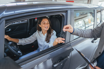 Happy Woman in Car Receiving Key From Salesperson at Car Dealership During Purchase