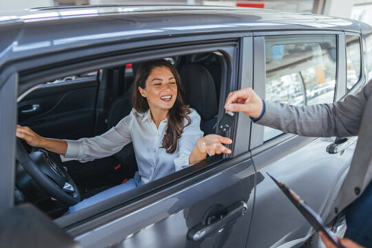 Happy Woman in Car Receiving Key From Salesperson at Car Dealership During Purchase