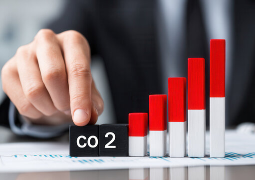 Rising CO2 levels shown through a hand placing blocks on a graph with red and white bars in an office setting