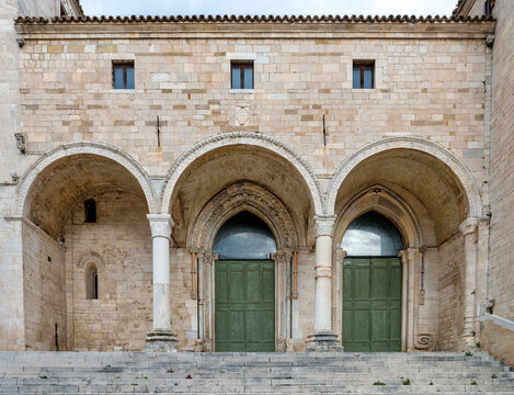 Editorial image of the fa&ccedil;ade of Osimo Cathedral in Italy, featuring Romanesque-Gothic architecture with a triple portico, arches, stone masonry, columns and pointed portals in a frontal view.