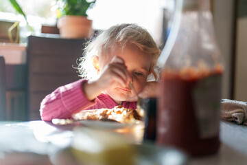 Child enjoying a meal at home during the afternoon with sunlight streaming in through the window