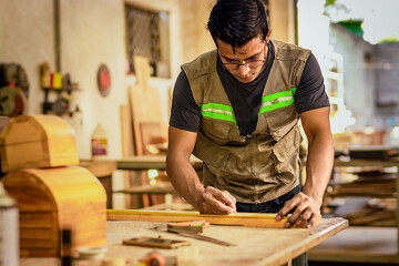 Carpenter with glasses taking measurements at the workbench. Young cabinetmaker measuring a piece with a tape measure in the workshop