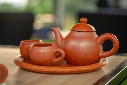 Traditional clay teapot and cups (Teh Poci) from Central Java on a tray. A rustic earthenware tea set, typical of Tegal culture, serving hot tea against a blurred background.