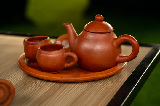 Traditional clay teapot and cups (Teh Poci) from Central Java on a tray. A rustic earthenware tea set, typical of Tegal culture, serving hot tea against a blurred background.