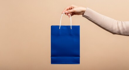 A human hand carefully presenting a small, vibrant blue paper shopping bag for retail purchase or gifting
