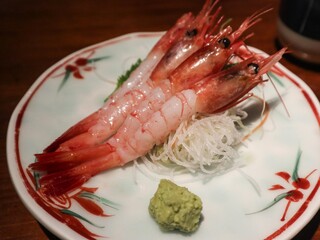 close up of Japanese raw uncooked three prawn sashimi with shell removed, on a floral plate and wasabi on the side
