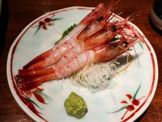 close up of Japanese raw uncooked three prawn sashimi with shell removed, on a floral plate and wasabi on the side