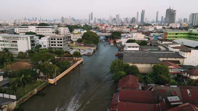 Aerial view of a longtail boat cruising along a bangkok canal, passing by wat paknam phasi charoen temple at sunset, Thailand.