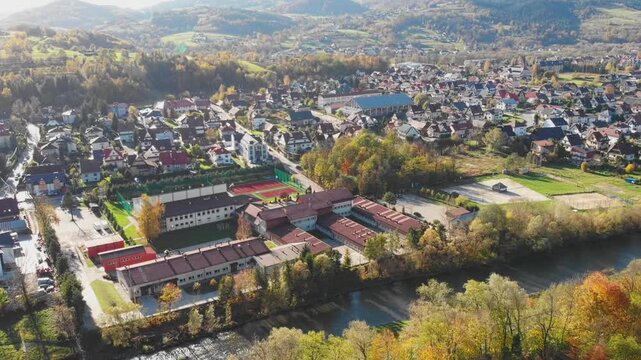 Aerial view of Mszana Dolna town center nestled in the Beskidy Mountains, Poland. Scenic autumn panorama featuring residential areas, river, and forested rolling hills.