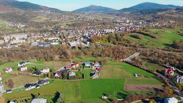 Aerial view of Mszana Dolna town center nestled in the Beskidy Mountains, Poland. Scenic autumn panorama featuring residential areas, river, and forested rolling hills.