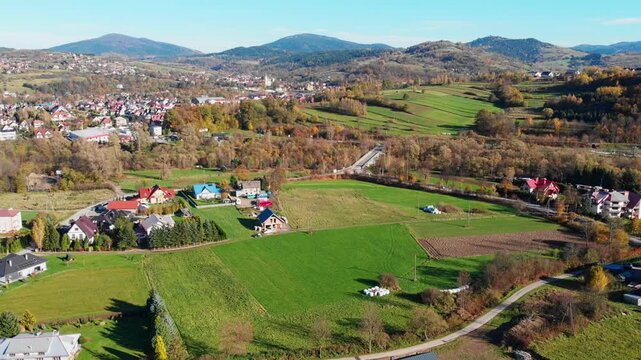 Aerial view of Mszana Dolna town center nestled in the Beskidy Mountains, Poland. Scenic autumn panorama featuring residential areas, river, and forested rolling hills.