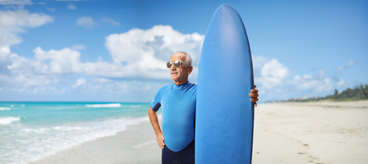Mature man in a wetsuit wearing sunglasses and holding a surfboard