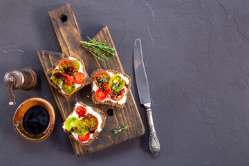 Bruschetta with cream cheese, cherry tomatoes on toasted bread on dark background top view copy space for text
