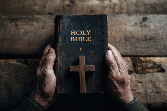 Hands holding an old Holy Bible with a wooden cross on a rustic wooden table