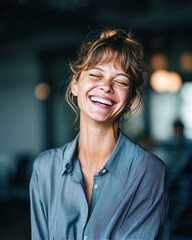 A joyful woman with a radiant smile, wearing a blue shirt, exudes happiness in a softly lit indoor environment.