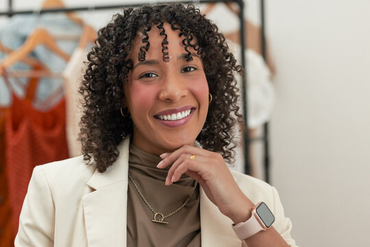 middle-aged woman wearing beige blazer smiling, posing at boutique clothing rack with orange dress